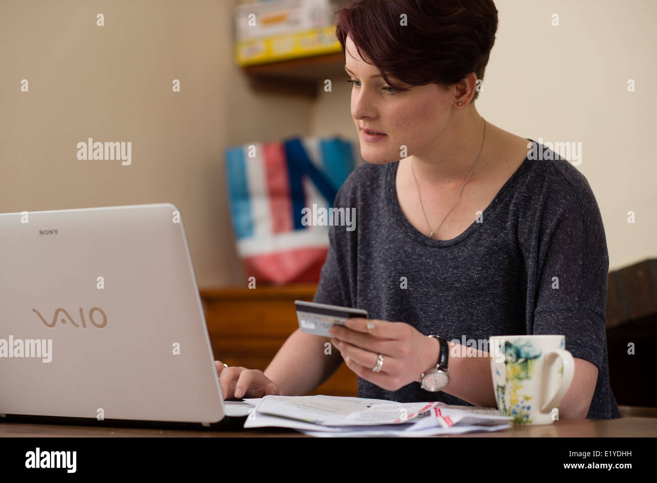 Eine junge Frau, die ihre Rechnungen online bezahlen mittels Laptop Computer und Kreditkarten-UK Stockfoto