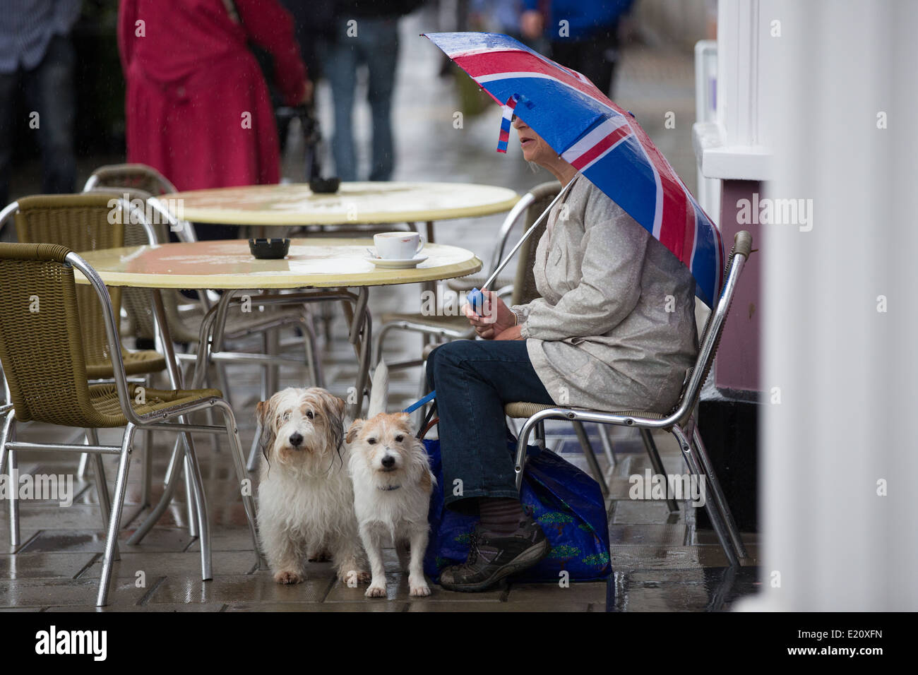 Eine Frau mit einem Union Jack Dach sitzt vor einem Café im Regen mit einer Tasse Tee. Stockfoto