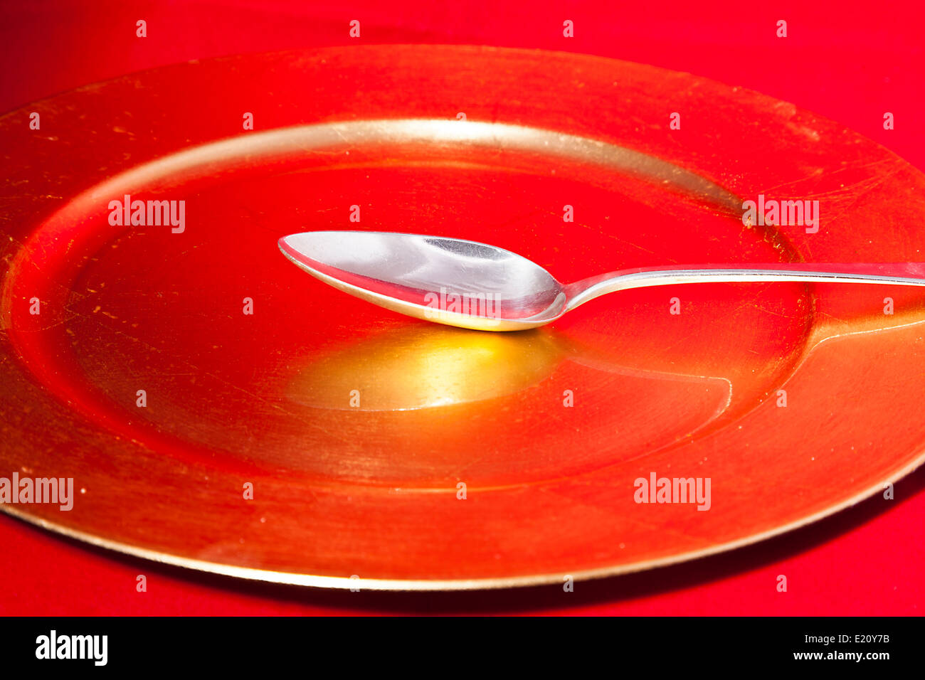Silberner Löffel auf einem Gold umrandeten roten Platte mit gold reflextion Stockfoto