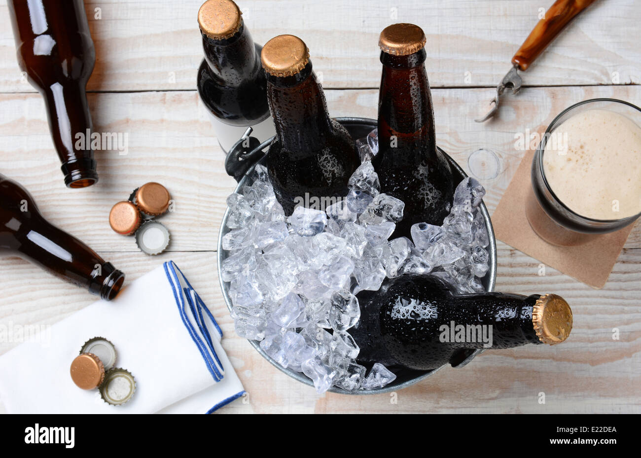 Hohen Winkel Schuss von einem Glas Bier mit einem Blecheimer mit ungeöffneten Flaschen. Die rustikalen Holztisch hat leere Flaschen Stockfoto