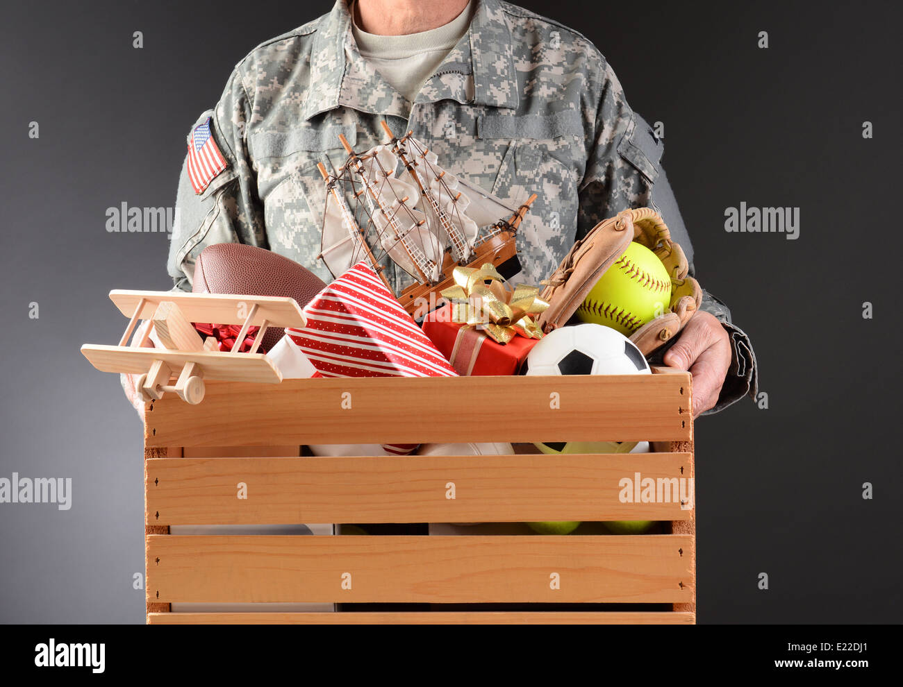 Nahaufnahme eines Soldaten in Strapazen hält eine Holzkiste voller Spielzeug und Sportgeräten für einen Urlaub Wohltätigkeitsaktion. Stockfoto