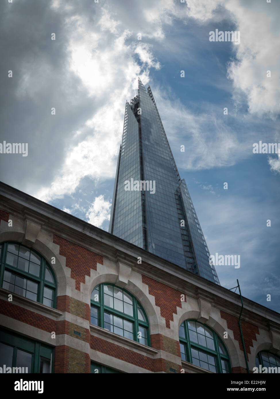 Ein Weitwinkel von The Shard London vor einem dramatischen blau-weißen Himmel mit Backsteinbau mit Rundbogenfenstern im Vordergrund Stockfoto