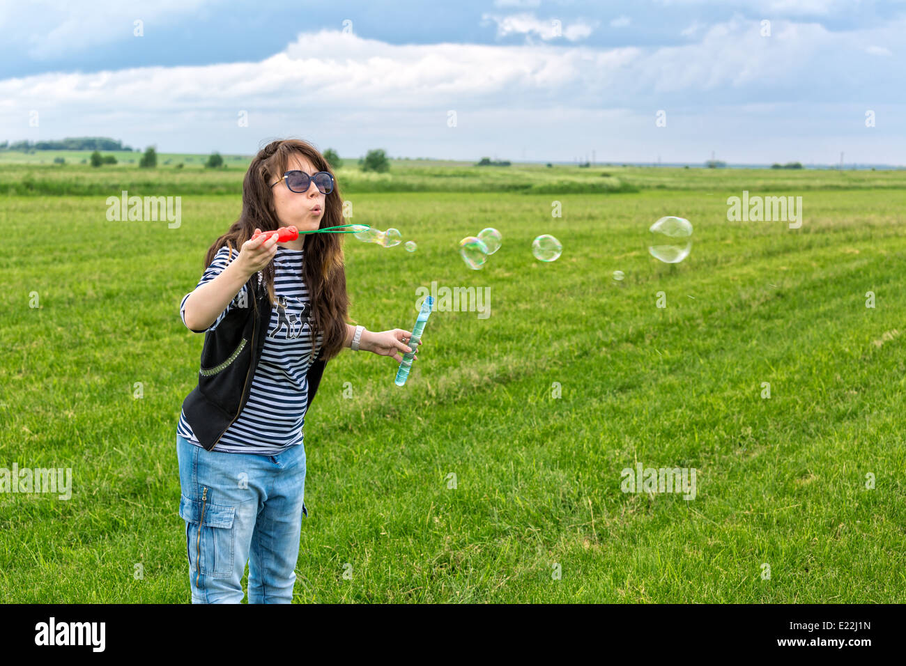 Schöne junge Frau machen Blowing Bubbles auf dem grünen Rasen Stockfoto
