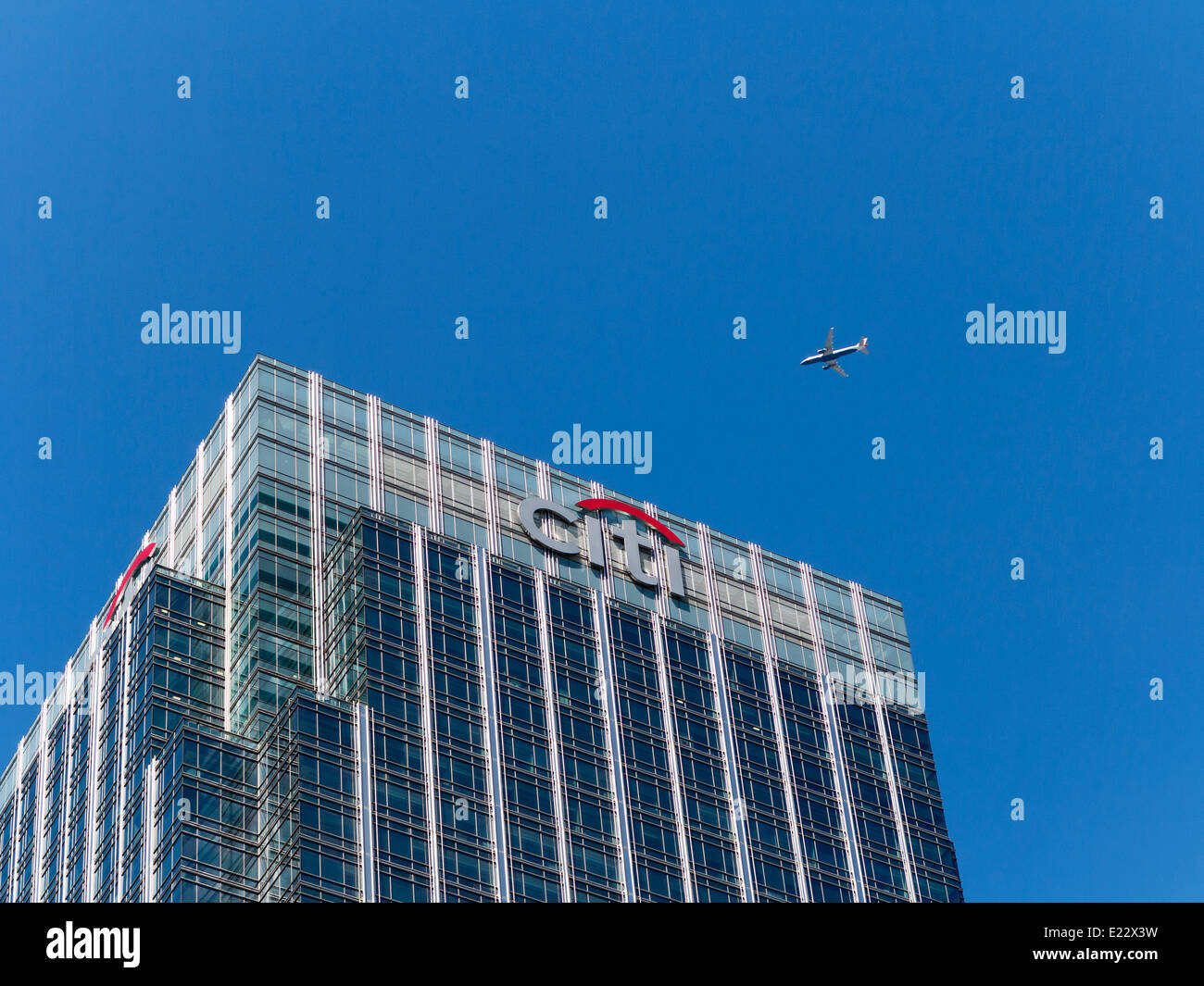 Blickte zu modernen Glas und Stahl stark reflektierende kommerzielle Wolkenkratzer vor blauem Himmel mit einem vorbeifahrenden Flugzeug Stockfoto