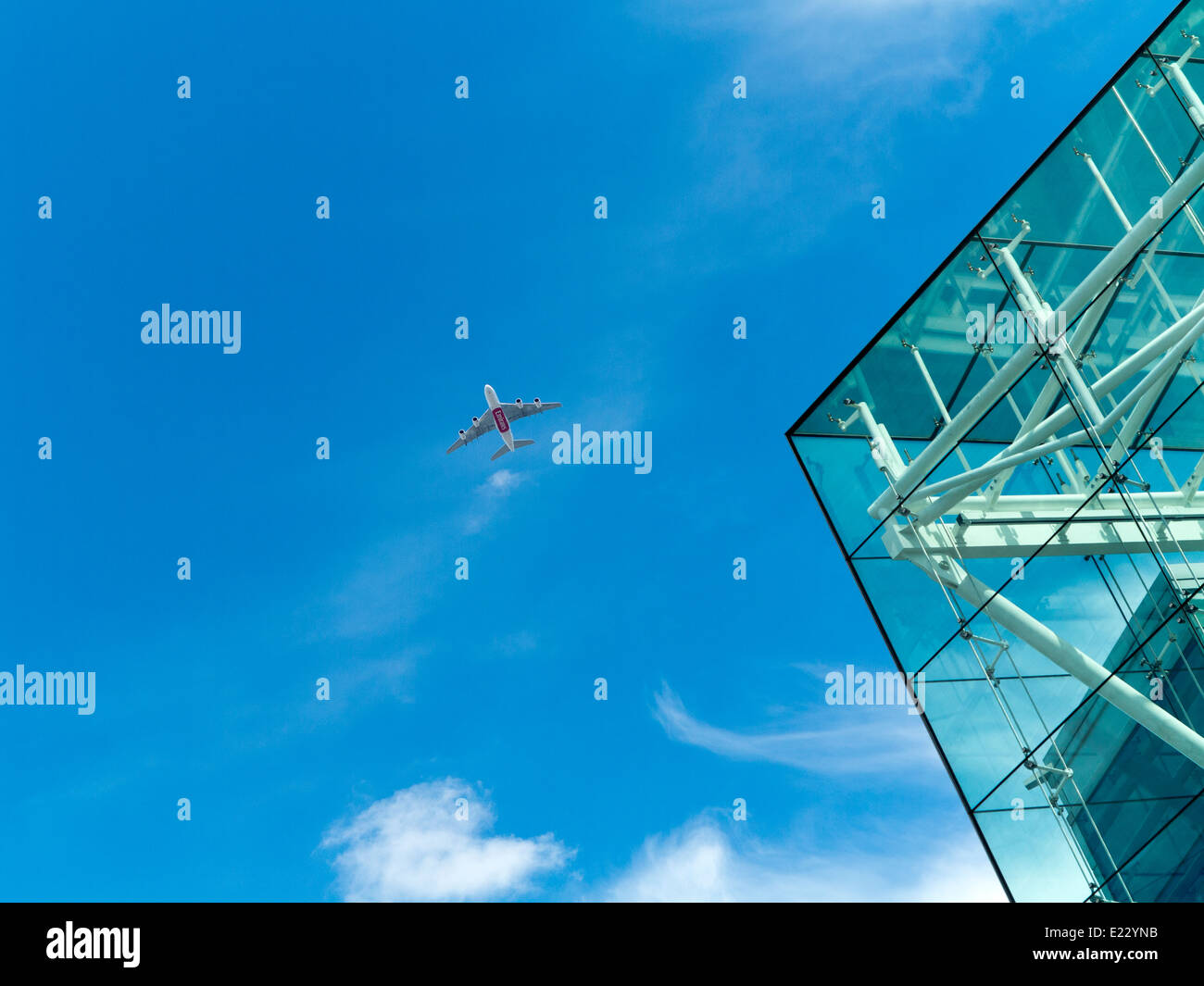 Emirates-Flugzeugen fliegt hoch in den blauen Himmel über die Ecke eines Wolkenkratzers Glas Stockfoto