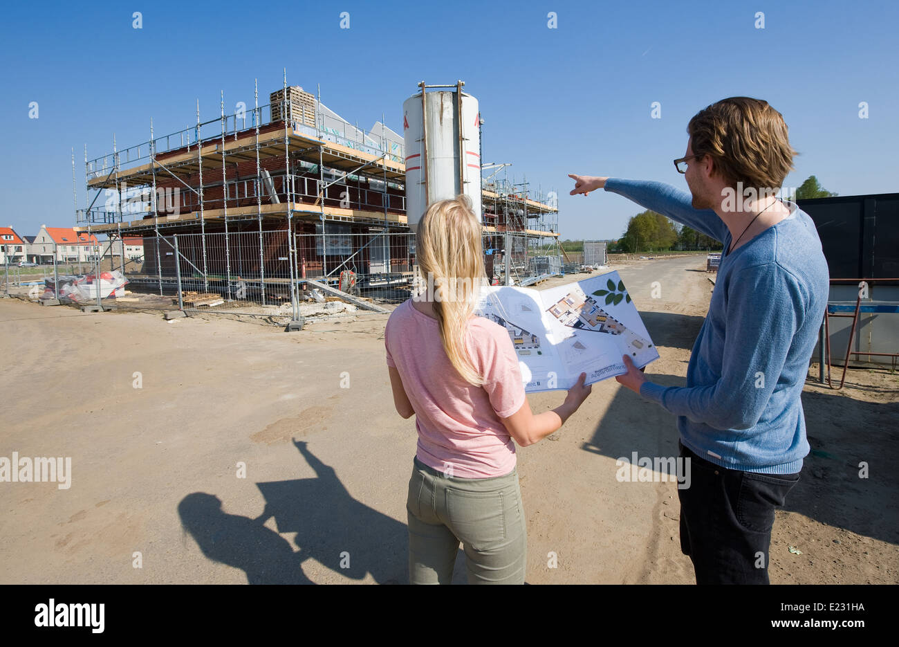 Junges Paar mit Blaupause, die auf der Suche wie ihr Haus gebaut wird Stockfoto