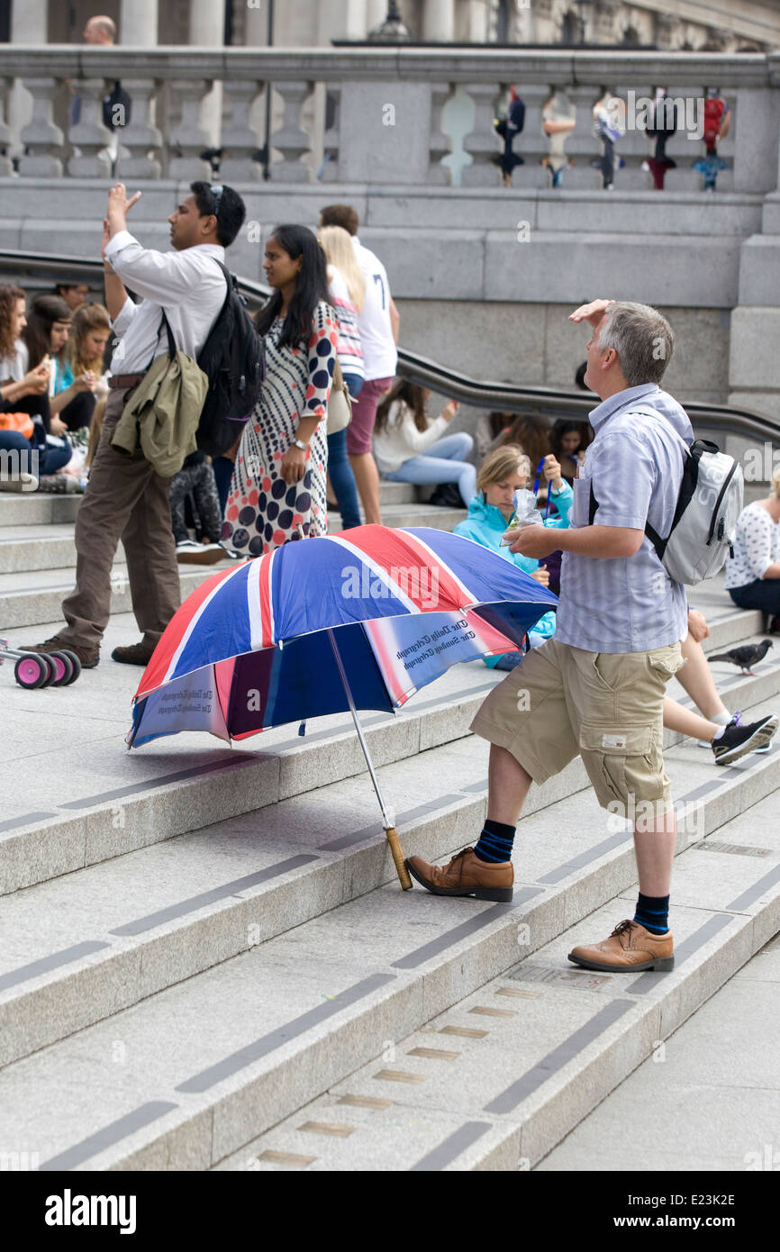 Touristen auf den Stufen am Trafalgar Square mit einem Union Jack-Schirm Stockfoto