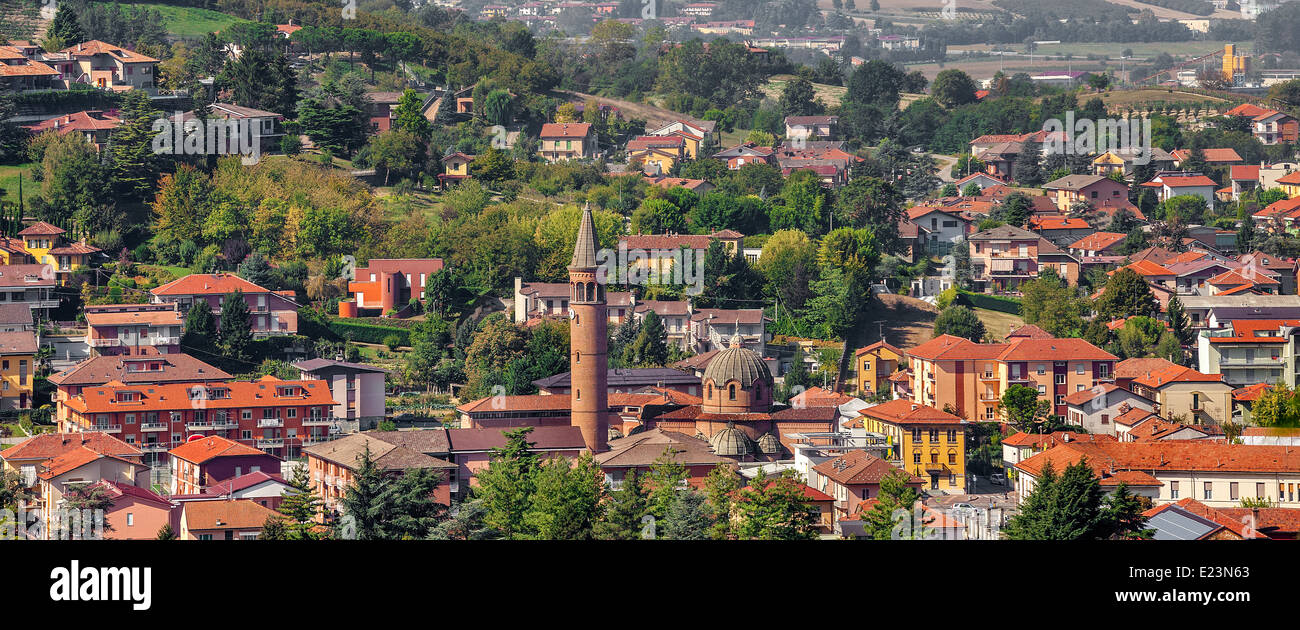 Blick auf den Glockenturm der Kirche zwischen Häusern und grünen Bäumen in der Stadt von Alba im Piemont, Norditalien (Panorama). Stockfoto