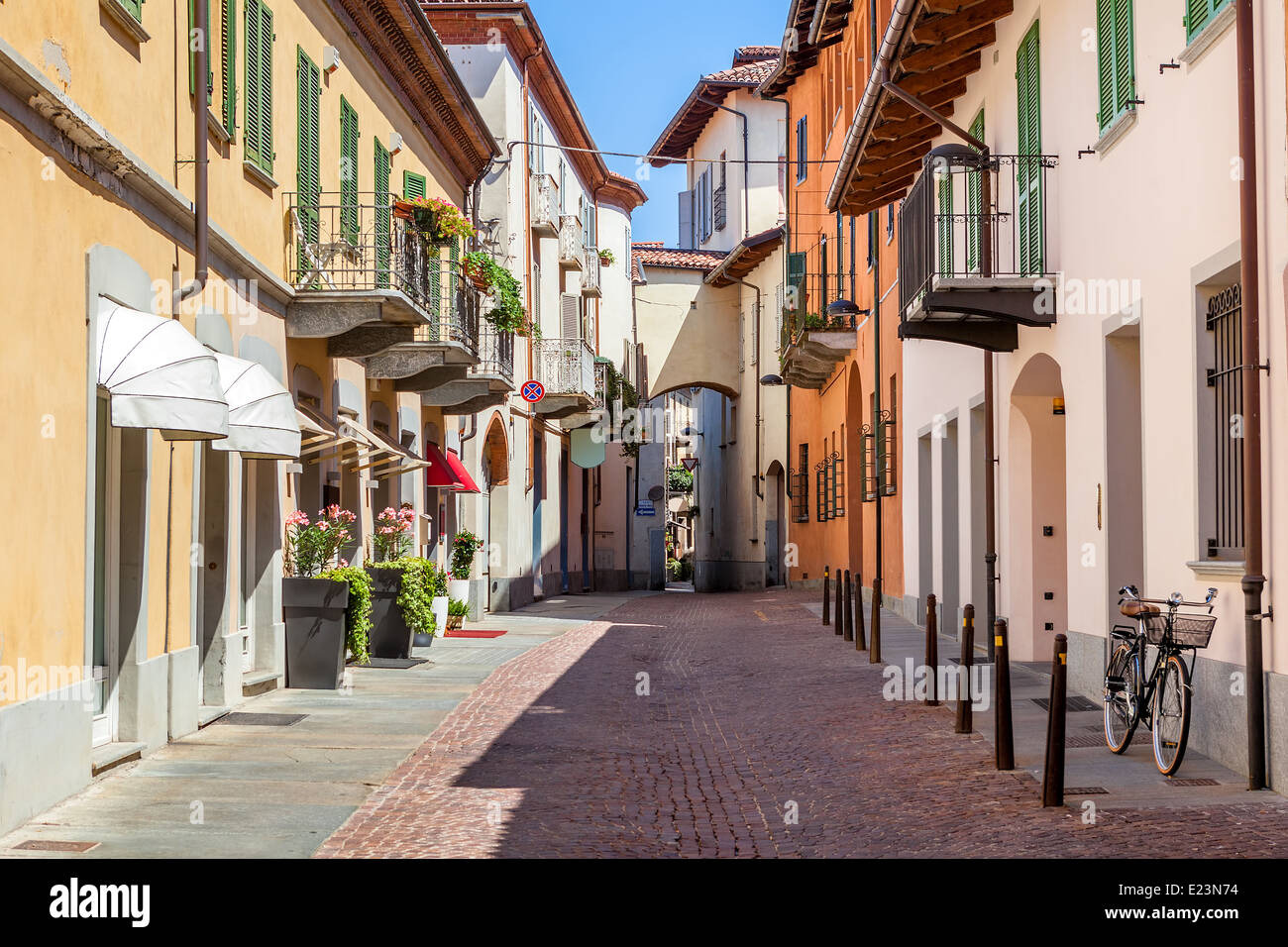 Blick auf leere schmale asphaltierte Straße zwischen bunten Häusern und Fahrrad lehnt an der Wand in Stadt von Alba, Italien. Stockfoto