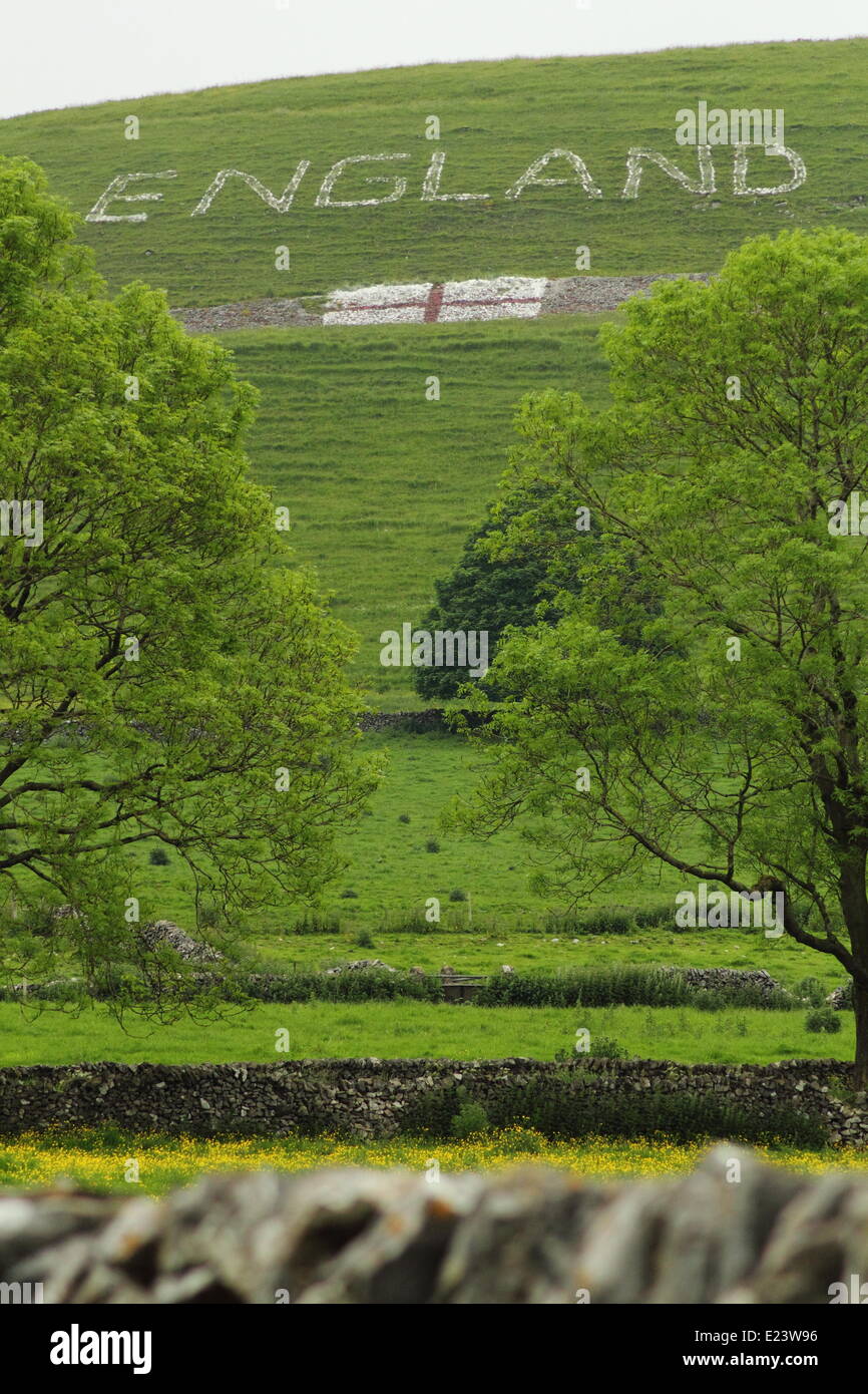 Peak District, Derbyshire, UK. 15. Juni '14. Ein Team von 15 Dorfbewohnern im Alter von sechs bis 70 Jahre alt - ein riesiges England Zeichen auf einem Hügel oberhalb des malerischen chelmorton in der Nähe von Buxton erstellt haben. Das geistesprodukt der lokalen Bewohner, phil Swindell, das Kunstwerk dauerte zwei Tage mit 15 Taschen von Kalk, rote Sprühfarbe und 10 Gallonen Leim. phil, 44, sagte, daß die Mannschaft eine Kette der Kalkstein Schriftzug in die Stellung auf dem Familienbesitz Land zu tragen. "Es ist eine große Aufgabe, wenn Sie dort oben," fügte er hinzu. chelmorton ist das höchstgelegene Dorf in Derbyshire und einer der höchsten in England. © Matthew Taylor/alamy Stockfoto