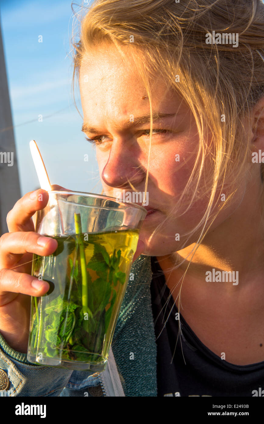 eine blonde und hübsche junge Frau trinken Pfefferminztee auf der Terrasse in der Sonne Stockfoto