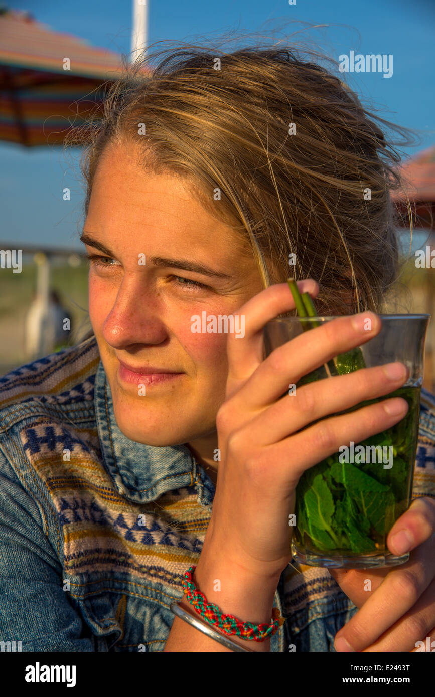 eine blonde und hübsche junge Frau trinken Pfefferminztee auf der Terrasse in der Sonne Stockfoto