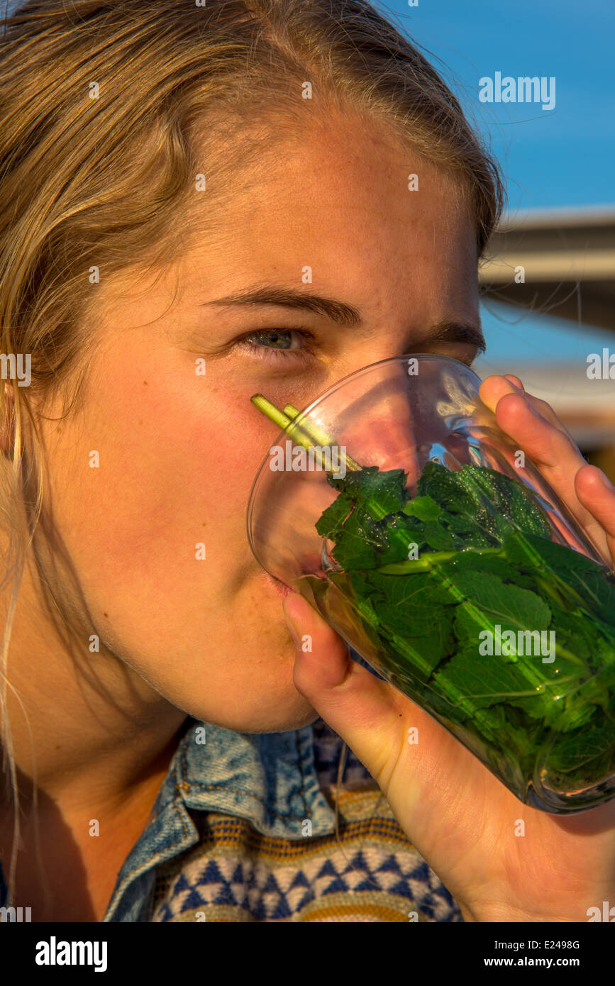 eine blonde und hübsche junge Frau trinken Pfefferminztee auf der Terrasse in der Sonne Stockfoto