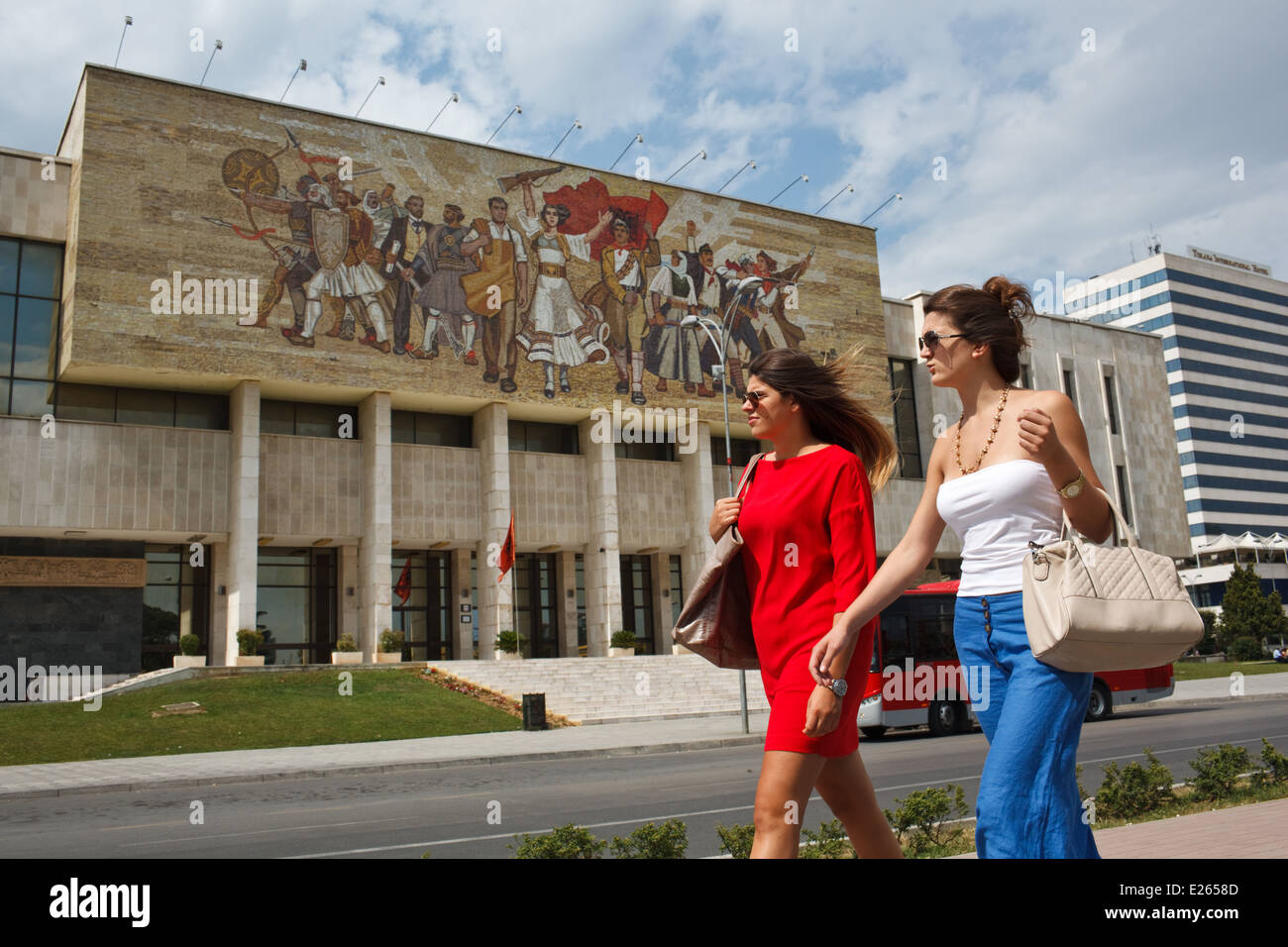 Zwei junge modische Frauen gehen vorbei an historischen Nationalmuseum am Skanderbeg-Platz, Tirana, Albanien. Stockfoto