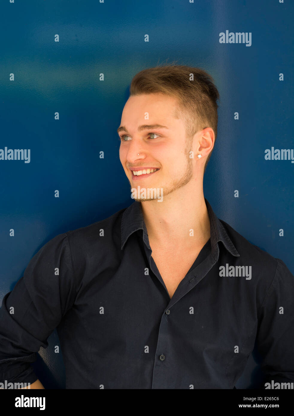 Attraktive Blond, blaue Augen junge Mann lächelnd und wegsehen, blau Metall Wand Stockfoto