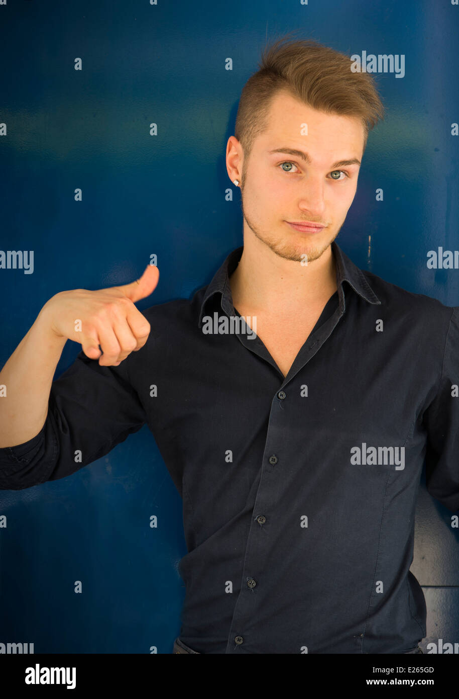Attraktive Blond, blaue Augen junge Mann lächelnd und Daumen Schild mit einer Hand zu tun. Blauer Hintergrund Stockfoto
