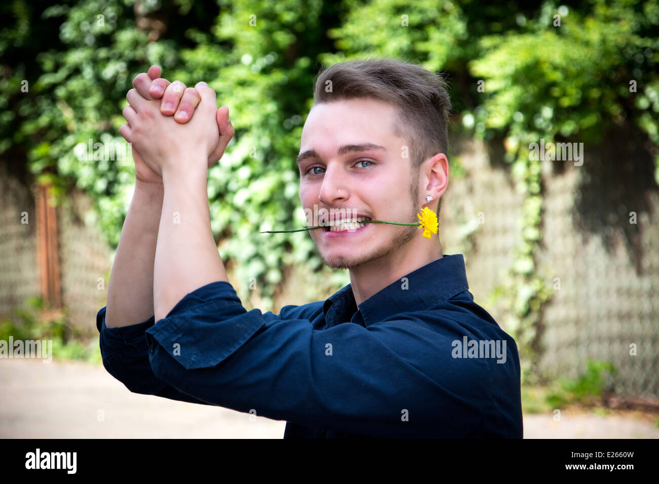 Hübscher junger Mann mit Blume im Mund klatschte. Im freien Stockfoto