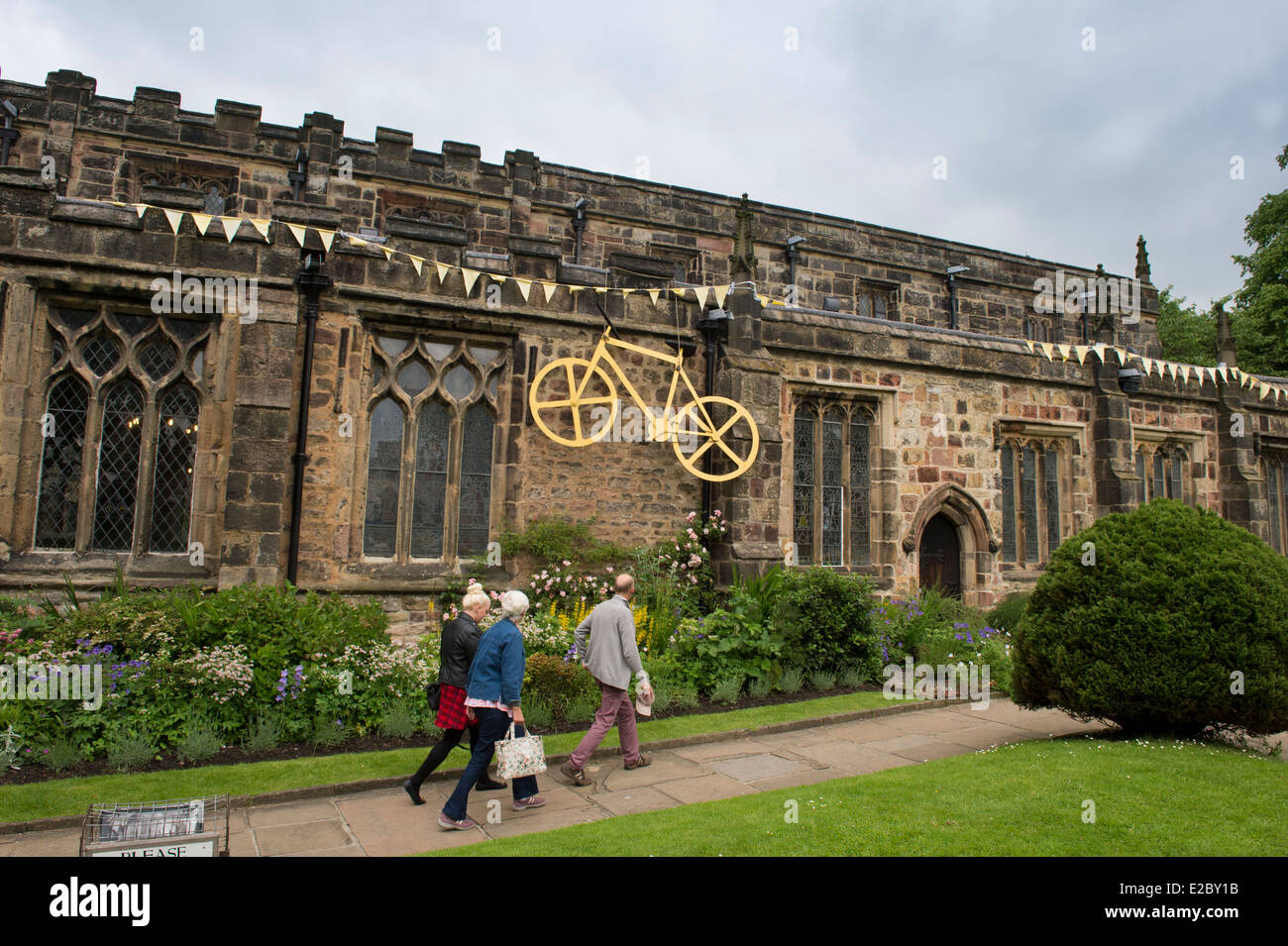 3 Personen vorbei an Kirche der Heiligen Dreifaltigkeit, Skipton, geschmückt mit großen, gelben Rad & Bunting flags feiern Tour de France - Yorkshire. England, UK. Stockfoto