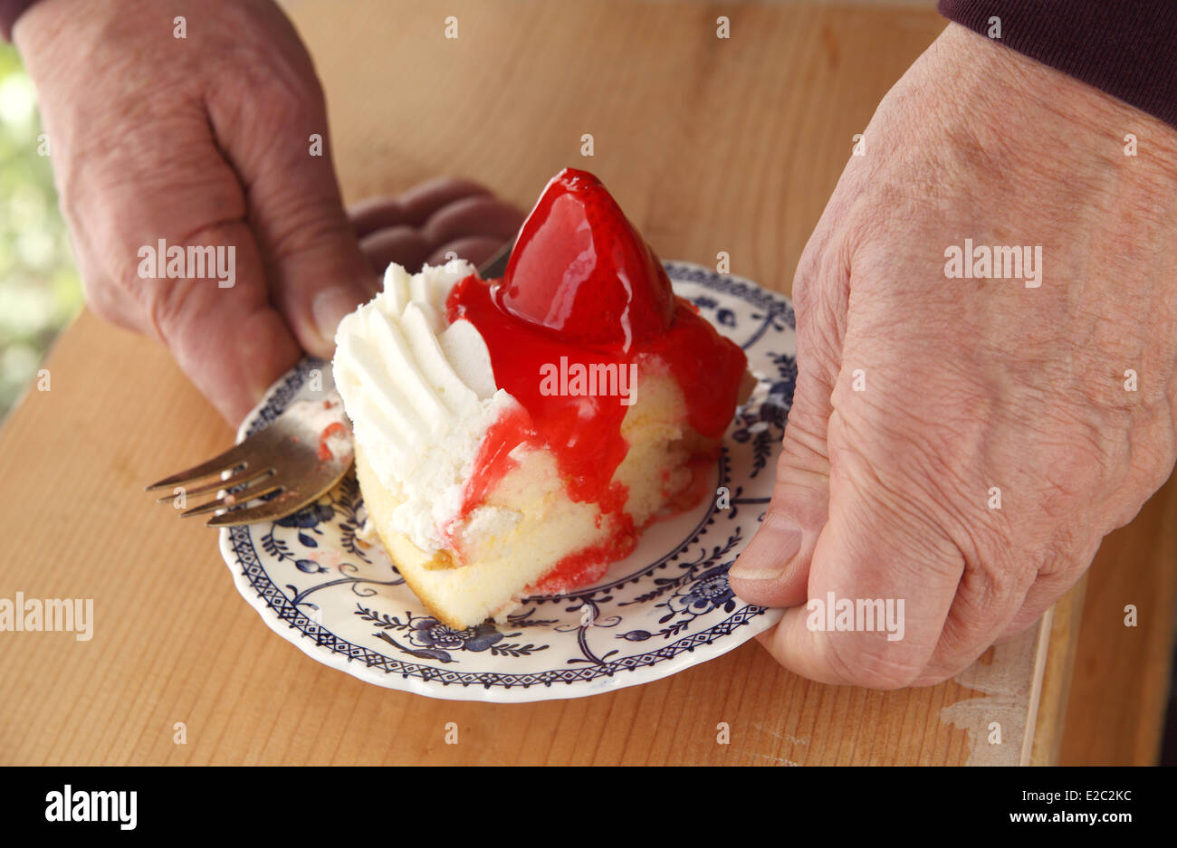 Mann mit frischem Erdbeer-Topping auf eine Portion Kuchen mit Schlagsahne dekoriert Stockfoto
