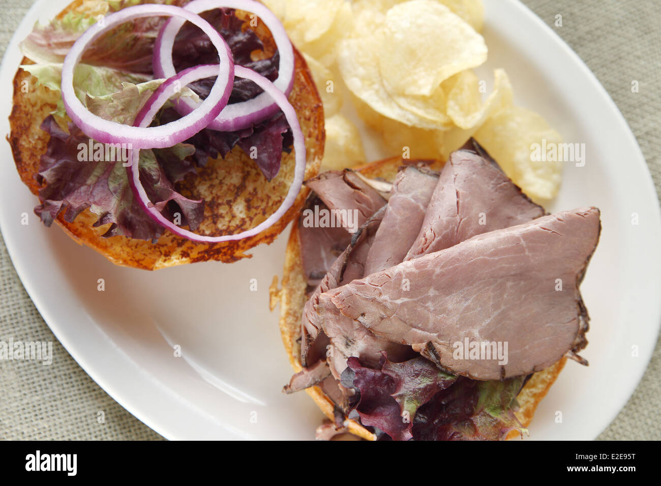 Scheiben Roastbeef und roten Zwiebeln auf einem getoasteten Brötchen mit Pommes frites Stockfoto