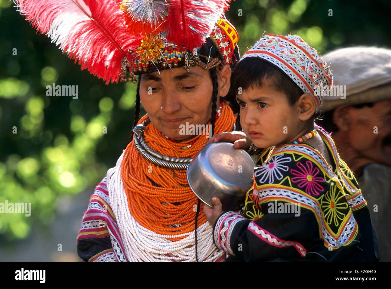 Pakistan Khyber Pakhtunkhwa Kalash Täler Bumburet Tal Kalash Frau mit einem Kind in armen geschmückt mit Federn auf ihren Kopfschmuck und herumtragen Hals eine Drehmoment traditionelle Nouristani Kette auf eine Kaskade von Perlenketten Wohlstand der ausstellenden Stockfoto