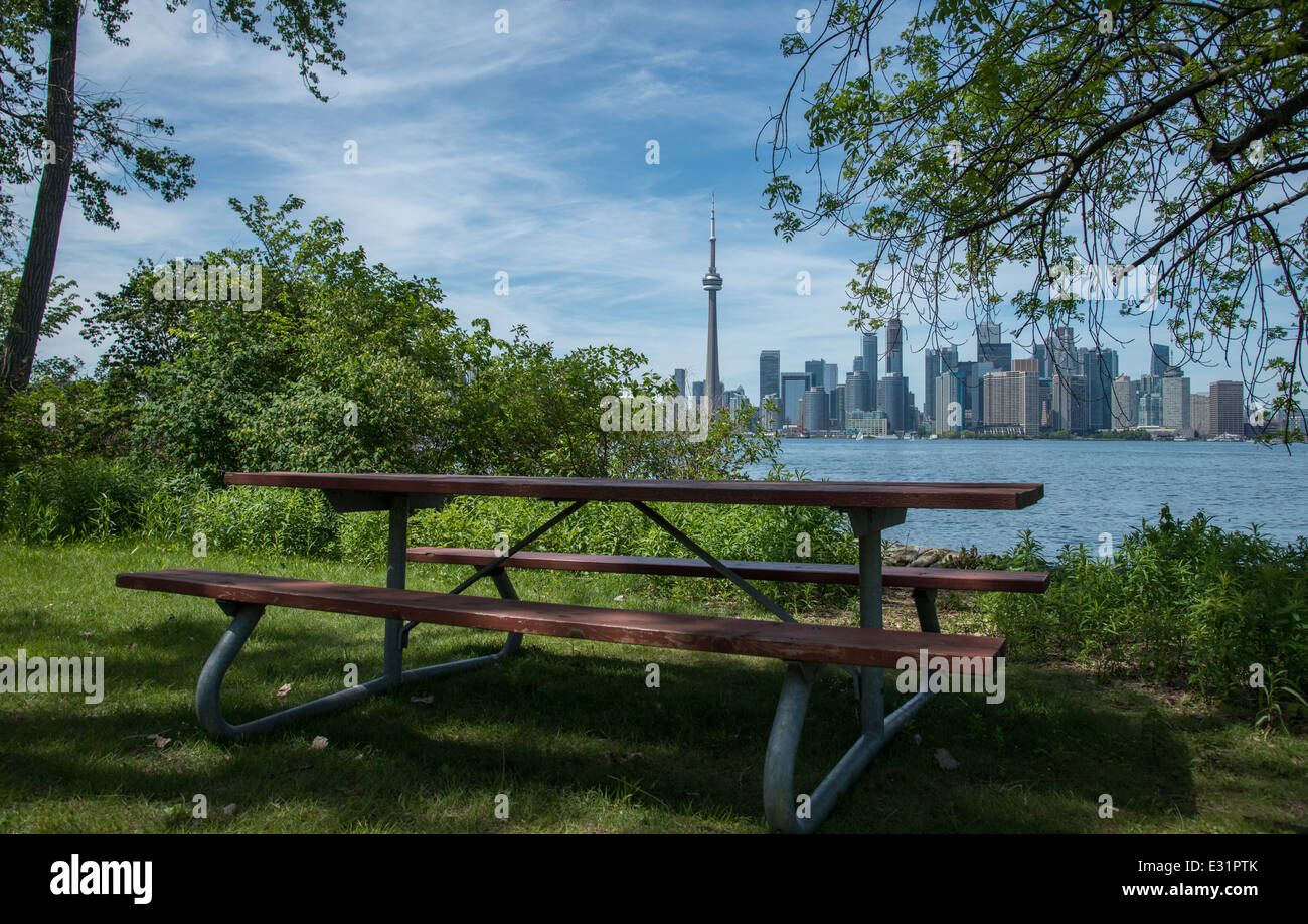 Ein Picknick-Tisch sitzt auf dem Rand des Toronto Island Park mit Blick auf den inner Harbour und die Skyline von Toronto. Stockfoto