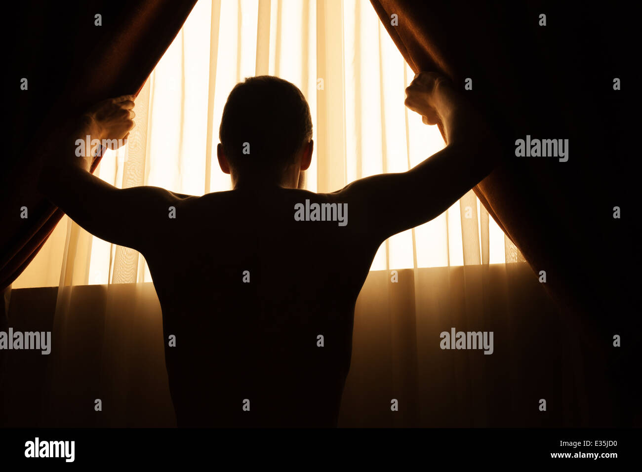Mann im dunklen Raum öffnet Vorhänge am Fenster, um das Licht des Morgens Stockfoto