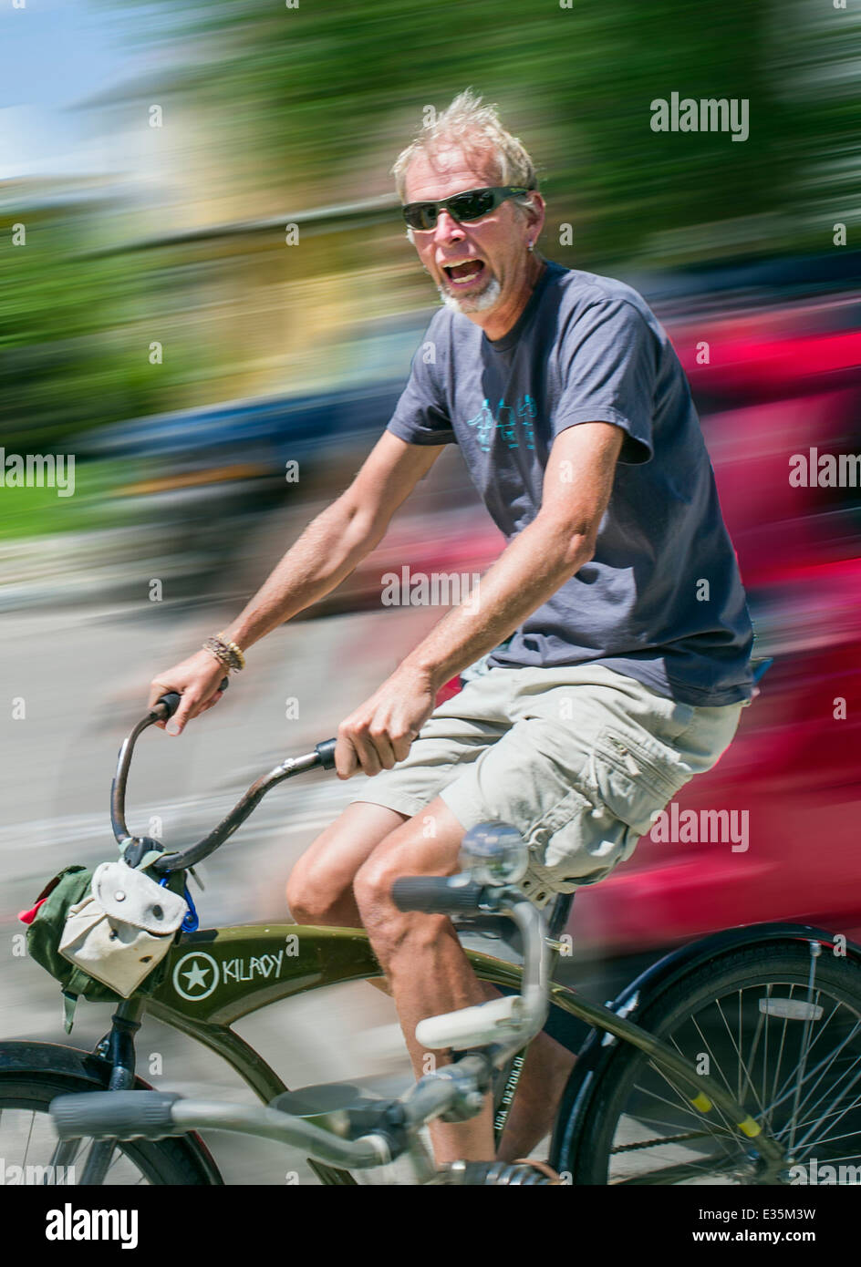 Glücklicher Mann lächelnd & Reiten eines Fahrrades an Sommertag in der kleinen Stadt Stockfoto