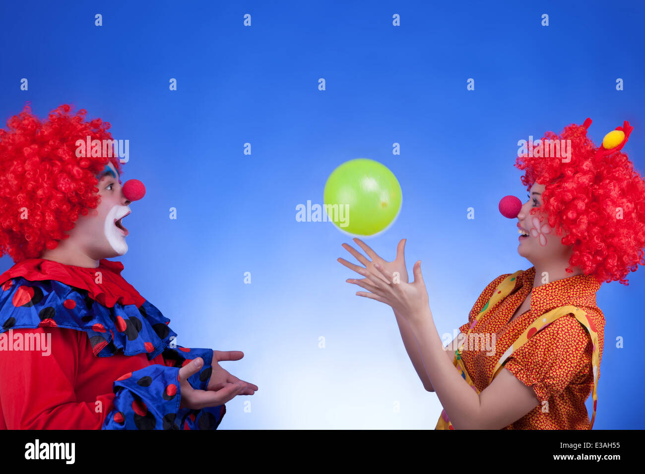 Clown-Paar spielt mit einem Ballon auf blauem Hintergrund. Professionelle Studiobeleuchtung. Lebendige Farben Stockfoto