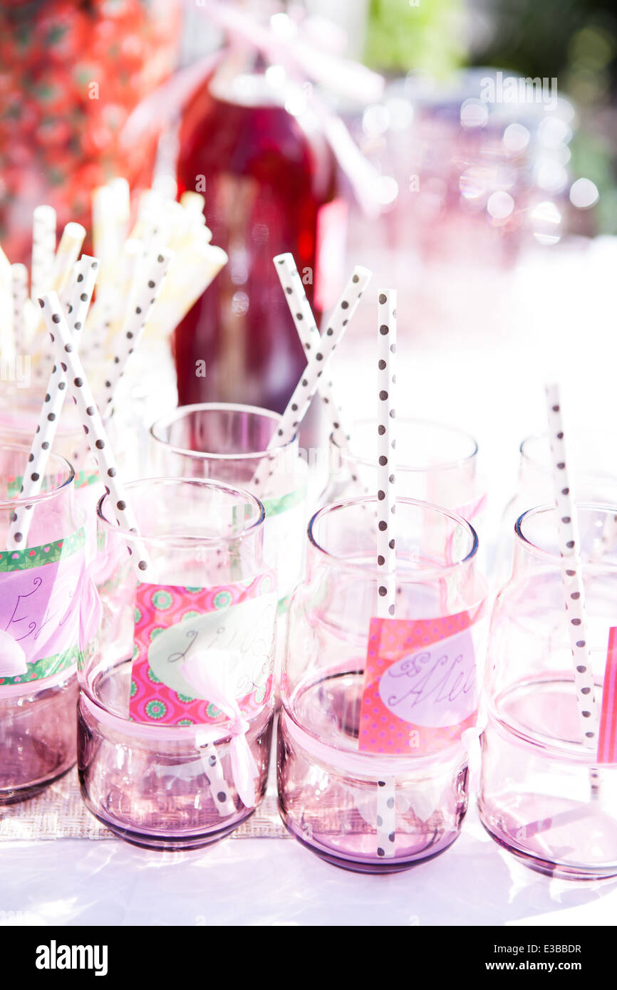 Nahaufnahme von dekorativen rosa farbigen Partei Gläsern mit Strohhalmen auf Tisch im Freien mit Flasche Fruchtsaft im Hintergrund Stockfoto
