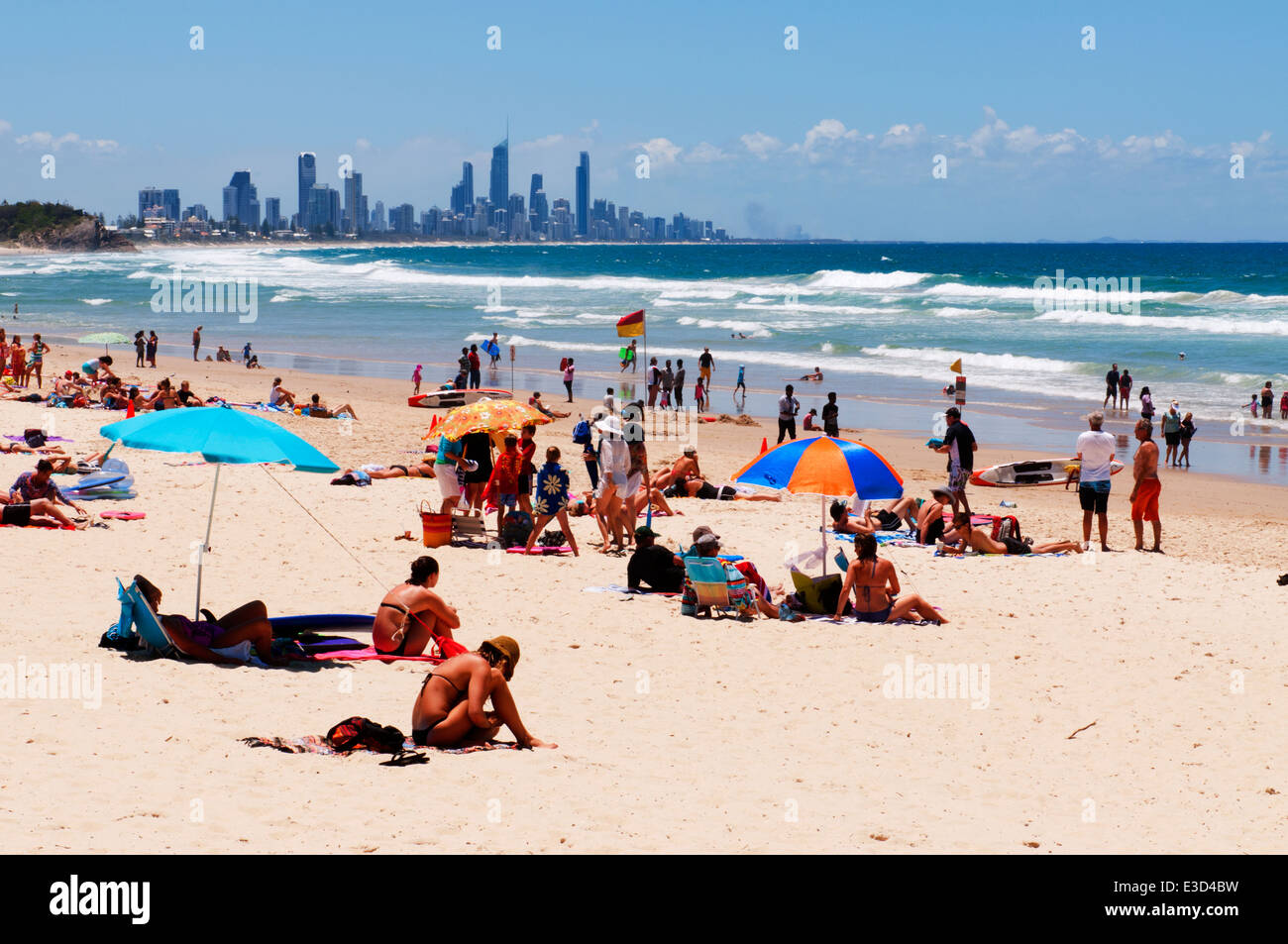 Sungathers am Kirra Beach mit der Skyline von Gold Coast in der Ferne. Stockfoto