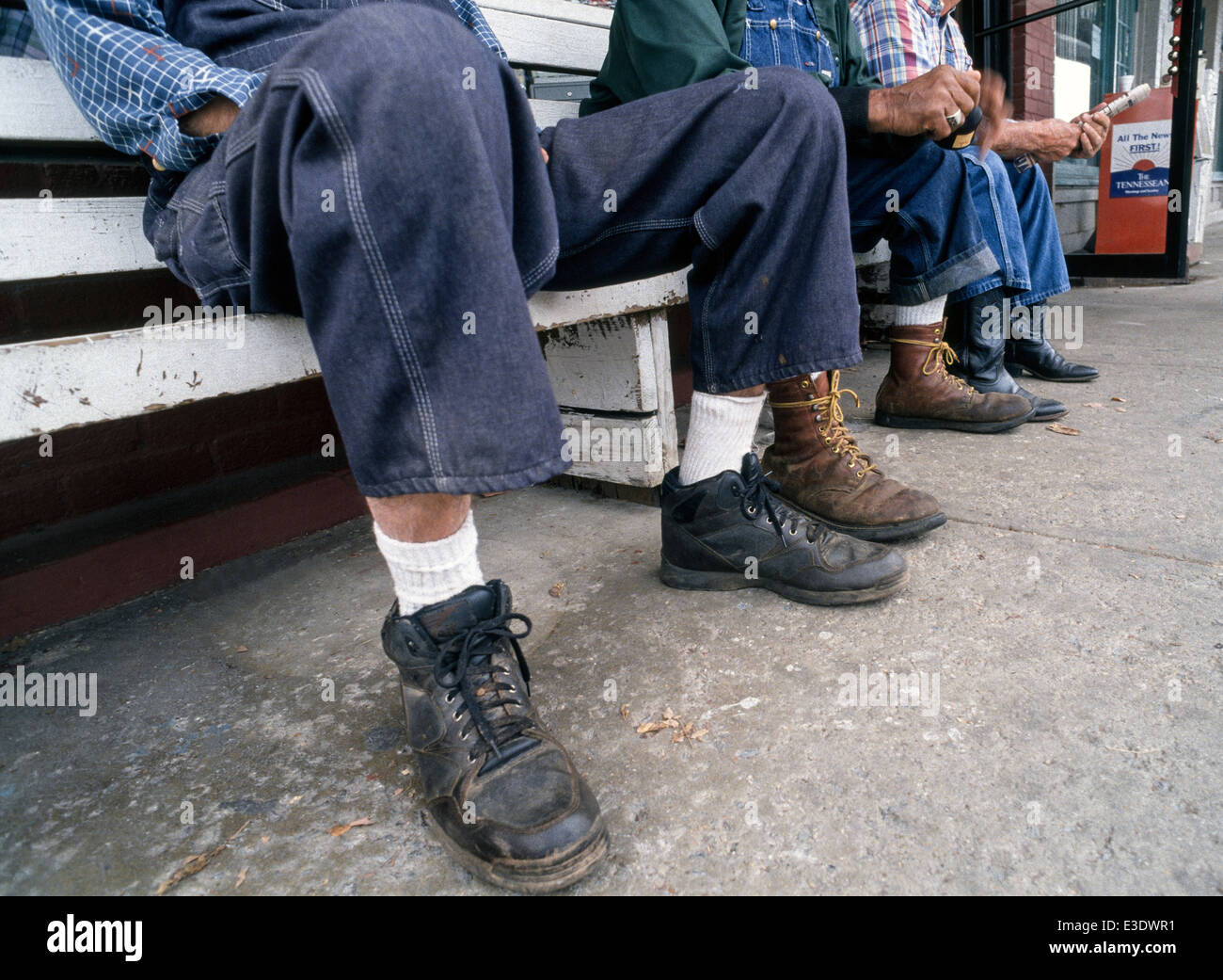 Pensionierte Landwirte in ihren blau-Jean Overall und Arbeitsstiefel entspannen und vertreiben uns die Zeit des Tages auf einer Bank vor einem Café in Lynchburg, Tennessee, USA. Stockfoto
