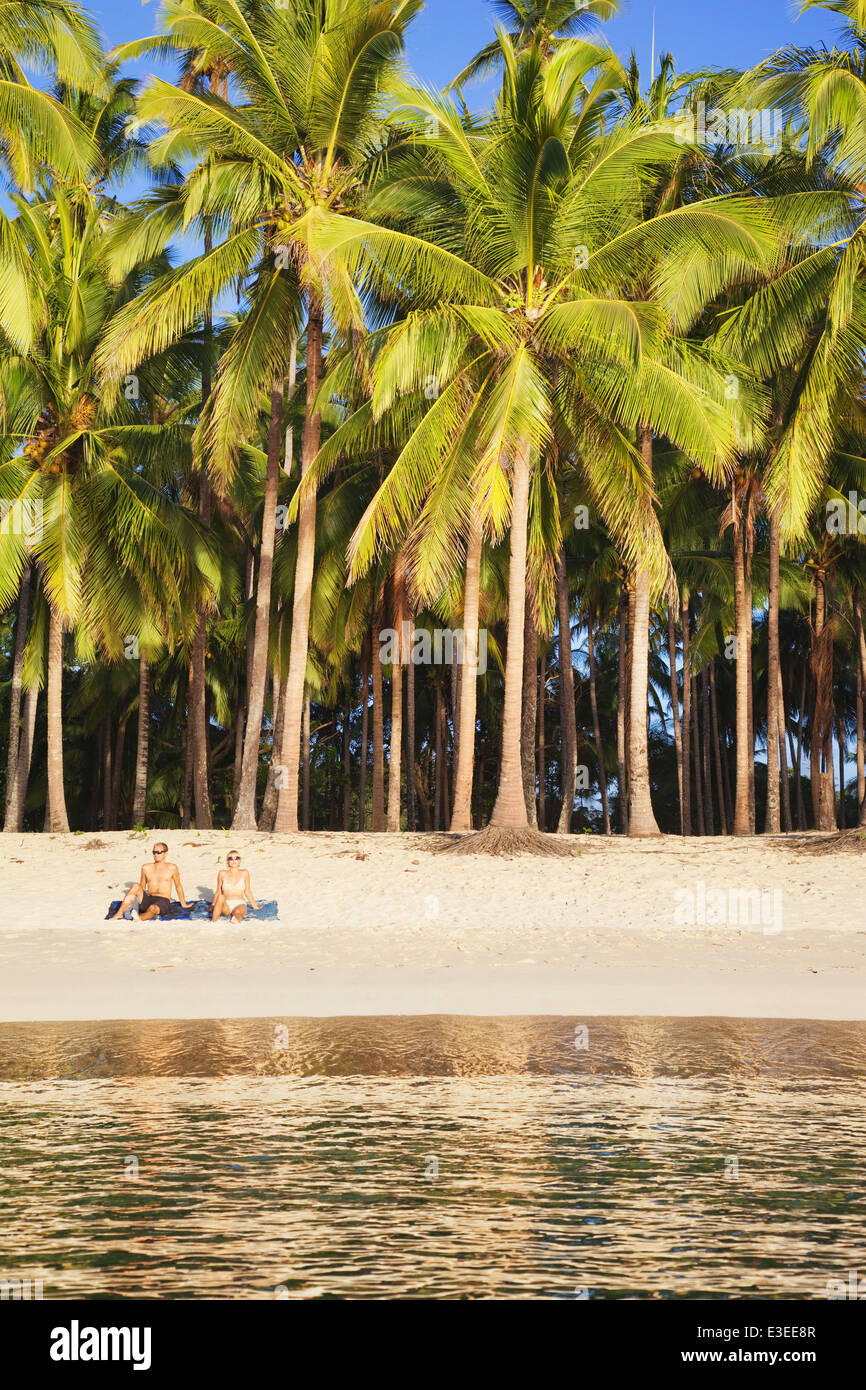 Zwei Menschen sitzen am Strand unter Palmen; Las Reetdächern; El Nido; Bacuit Bay; Palawan; Philippinen Stockfoto