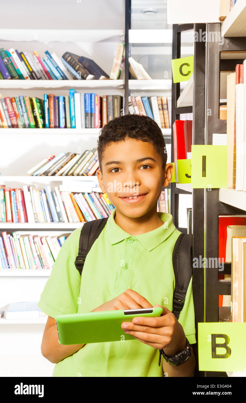 Lächelnde junge spielt mit Tablette in der Bibliothek Stockfoto