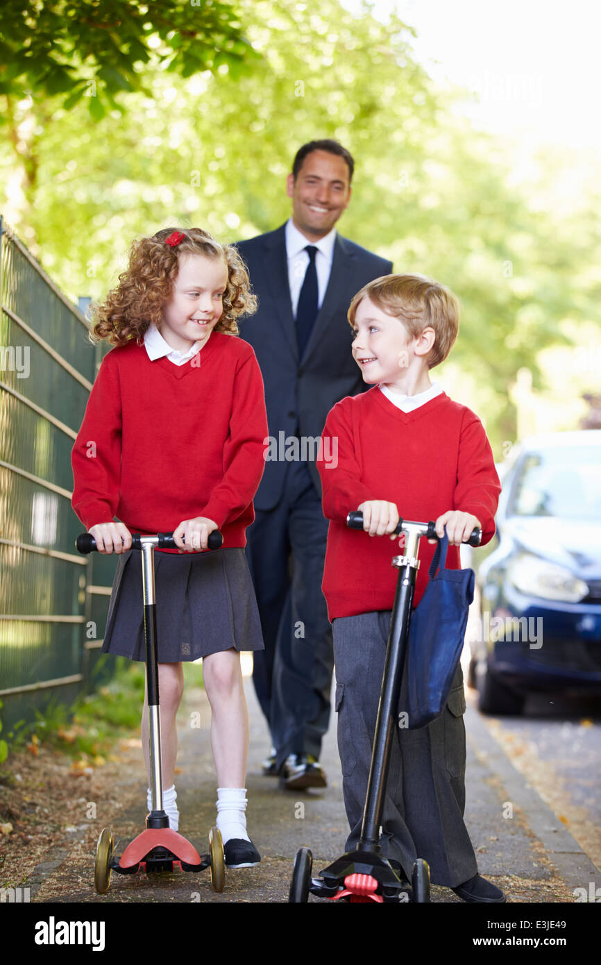 Kinder reiten Roller auf dem Weg zur Schule mit Vater Stockfoto