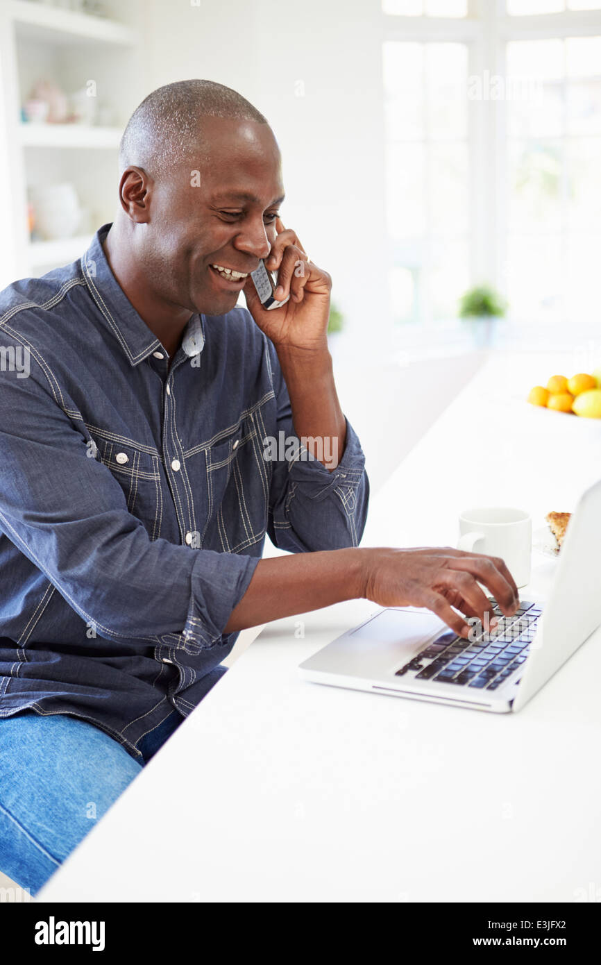 Mann mit Laptop und Gespräch am Telefon In der Küche zu Hause Stockfoto