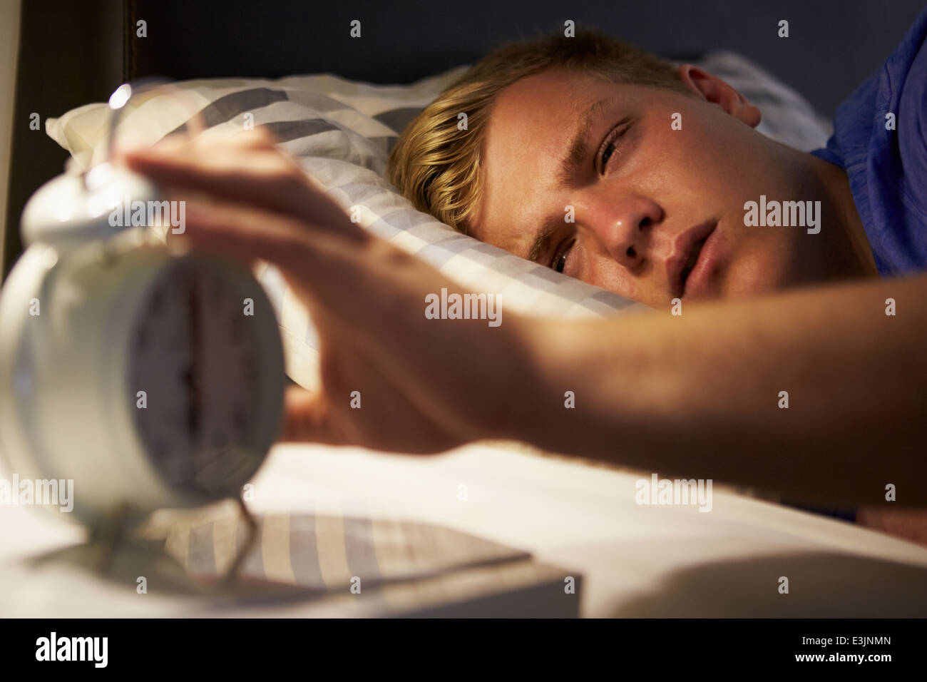 Teenager Waking Up im Bett und Wecker ausschalten Stockfoto