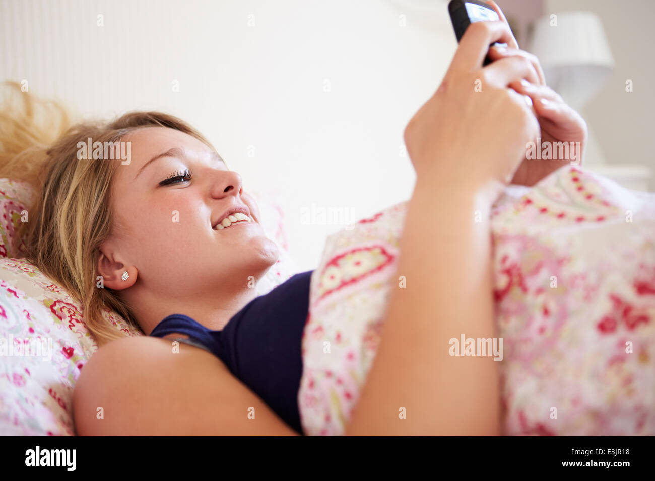 Teenager-Mädchen senden SMS, während im Bett liegend Stockfoto