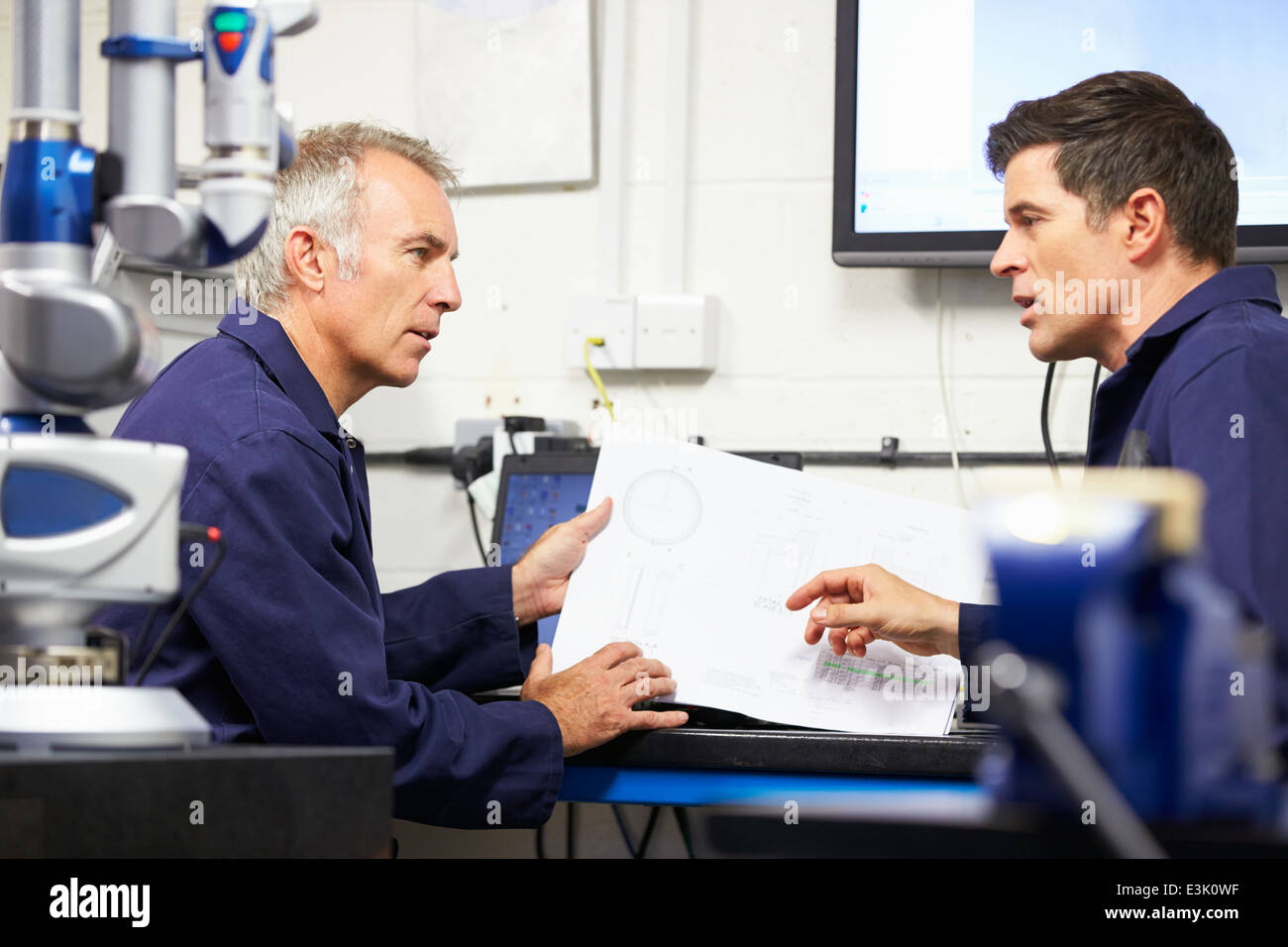 Zwei Ingenieure diskutieren Pläne mit CMM-Arm im Vordergrund Stockfoto