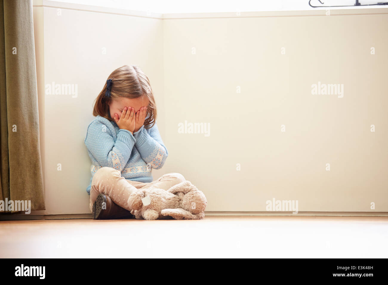 Unglückliches Kind zu Hause auf Boden In der Ecke sitzen Stockfoto
