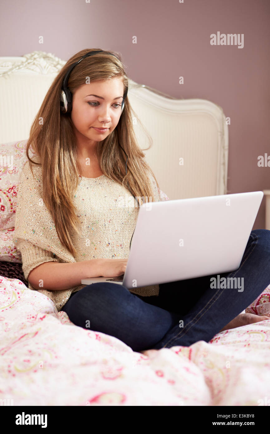 Teenager-Mädchen auf Bett mit Laptop mit Kopfhörern Stockfoto