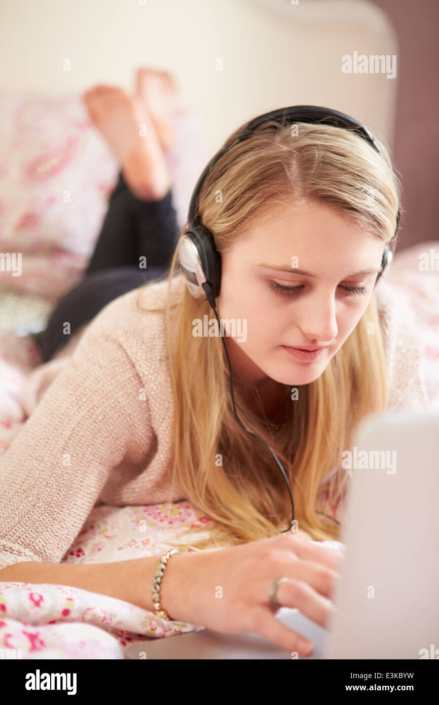 Teenager-Mädchen auf Bett mit Laptop mit Kopfhörern Stockfoto