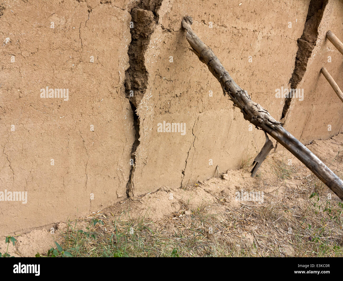 Eine rissige und Neigung Abschnitt der Lehmziegel-Mauer wird unterstützt durch eine hölzerne Stütze Stockfoto
