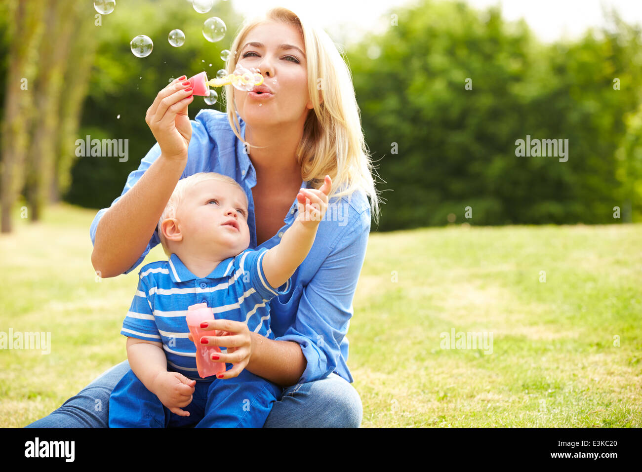 Mutter bläst Seifenblasen für Jungen im Garten Stockfoto