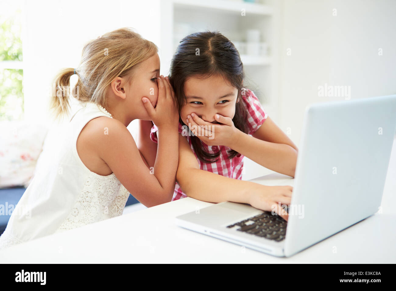 Zwei junge Mädchen mit Laptop zu Hause und Flüstern Stockfoto