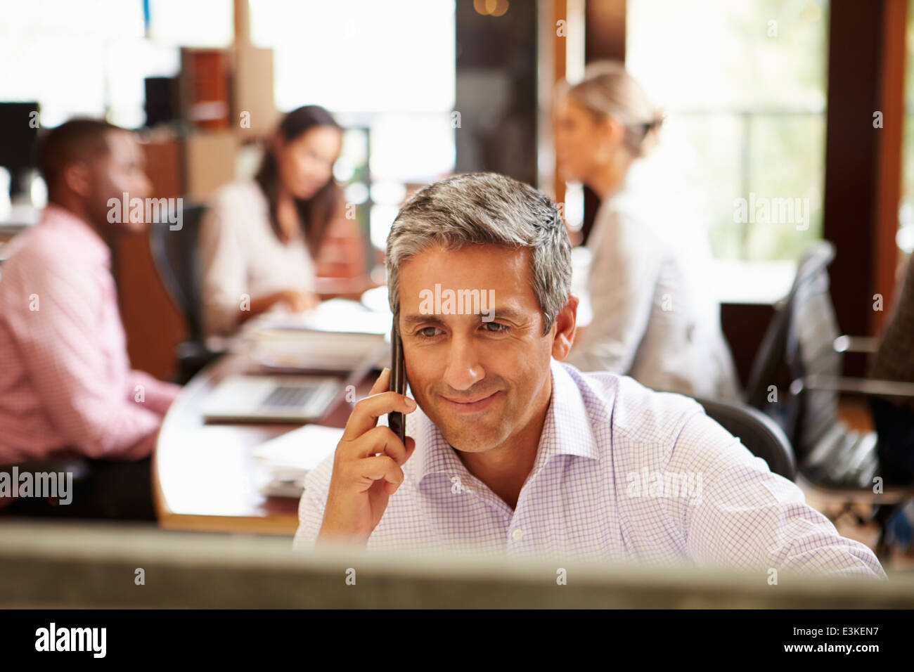 Geschäftsmann am Telefon am Schreibtisch mit treffen im Hintergrund Stockfoto