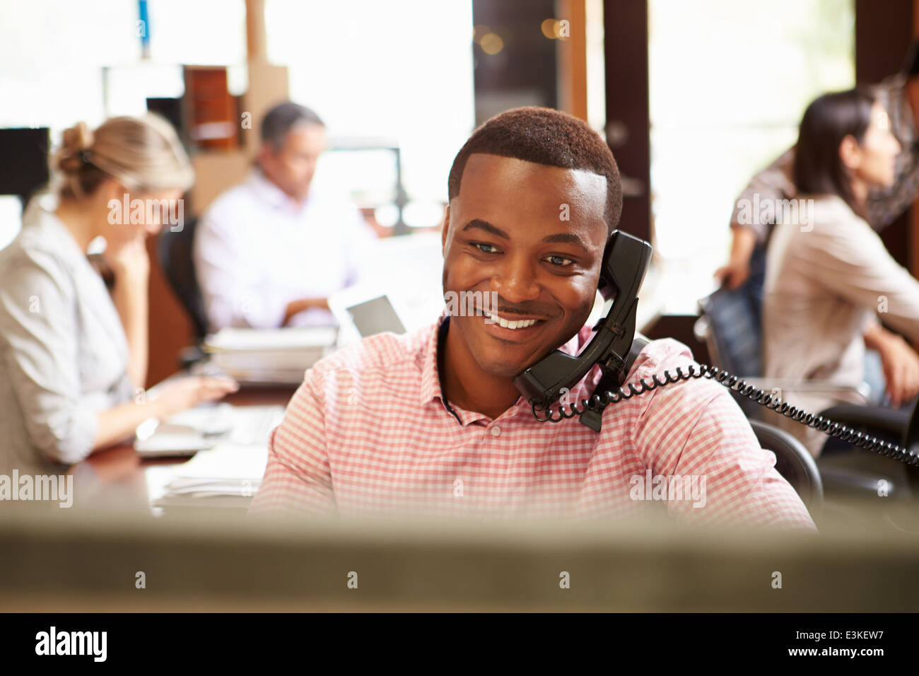 Geschäftsmann am Telefon am Schreibtisch mit treffen im Hintergrund Stockfoto