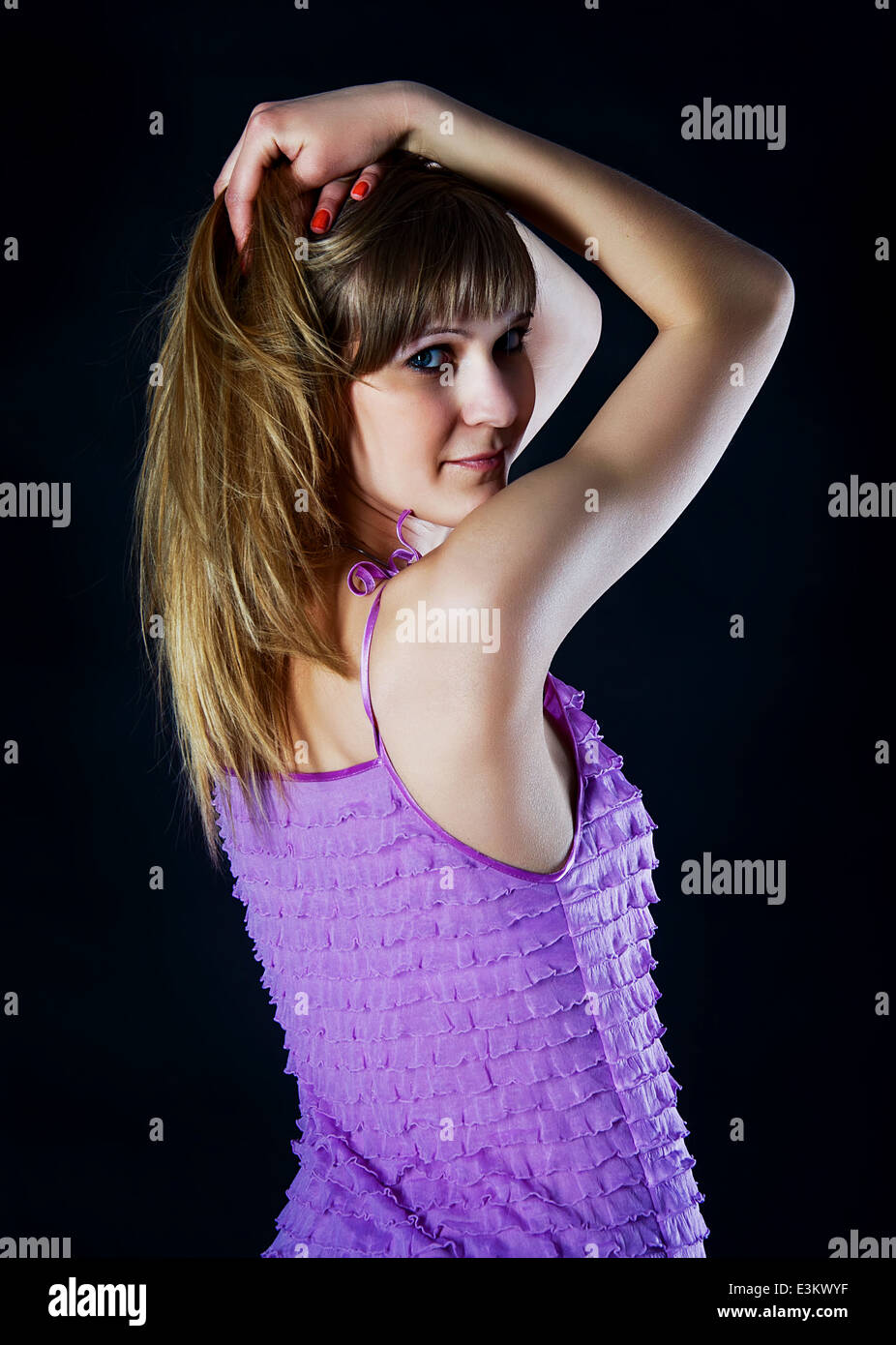 Schönes europäische Mädchen hält ihre blonden Haare und Rückblick auf schwarzem Hintergrund violett, lila, rosa Kleid Stockfoto