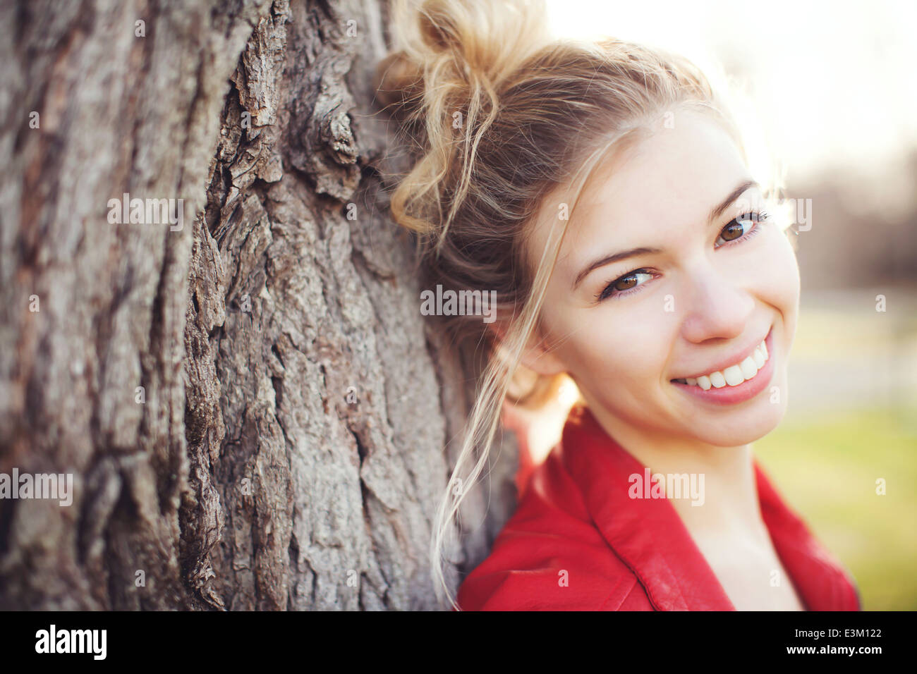 Porträt der jungen Frau (18-19) lächelnd stützte sich auf Baumstamm Stockfoto