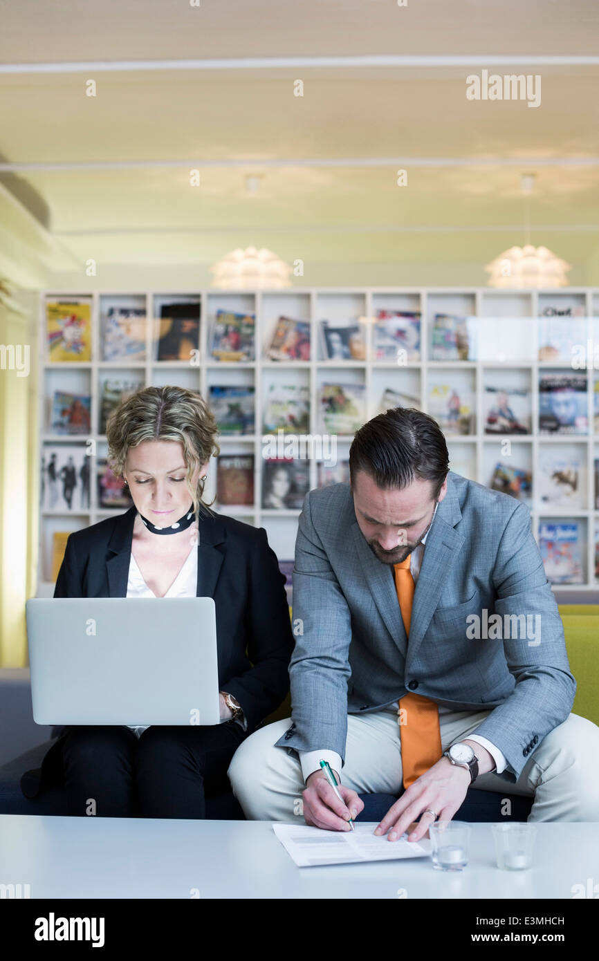 Reife Geschäftsfrau mit Laptop beim Kollegen unterschreiben in Kreativbüro Stockfoto